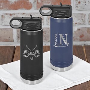 May include: Two personalized water bottles. One is black with "Richard" and golf club graphics. The other is blue with "Nathan" and an initial "N". Both have black lids and silver bases.