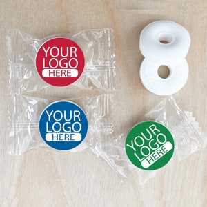 May include: Three individually wrapped packs of round mints with a hole in the center. Each pack has a round sticker with the text "YOUR LOGO HERE" in white letters on a colored background. The colors are red, blue, and green.