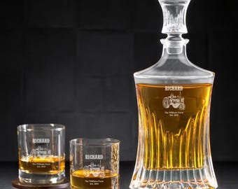 May include: A clear glass decanter and two matching glasses filled with amber liquid. The decanter and glasses are etched with a tractor design and the name "Richard". The decanter has a decorative stopper. The glasses sit on a dark surface.