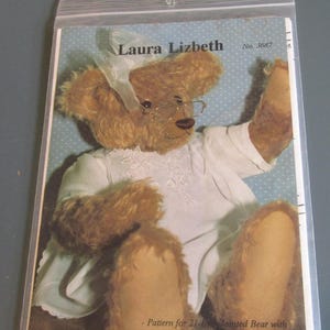 May include: A pattern for a 21-inch jointed bear named Laura Lizbeth, wearing glasses and a white dress. The pattern includes instructions for an armature, felt pads, and a 1930s style dress. The bear is made for mohair or fur fabric.