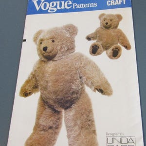 May include: Vogue Patterns 8658 Craft sewing pattern envelope featuring a tan plush teddy bear with a dark nose and paw pads. The design is by Linda Carr and shows a large standing bear and a smaller seated bear on the front cover of the paper packet.