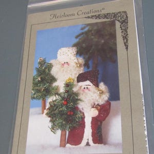 May include: A package featuring a Christmas craft pattern. The image shows two Country Santa figures, one in a red coat and one in a white coat, each holding a small Christmas tree. The text reads "#164 Nicki 9" Country Santa."