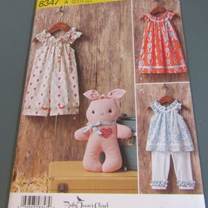 May include: Simplicity sewing pattern 8347 for children's clothing and a stuffed animal. The envelope displays a dress with a red tulip print, a dress with a white and red pattern, and a top with blue floral print paired with white ruffled pants.