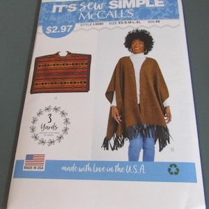 May include: A McCall's sewing pattern envelope for style L9580, labeled It's Sew Simple. The front displays two poncho designs: one with a horizontal striped pattern and another in solid brown with black fringe, available in sizes XS to XL.