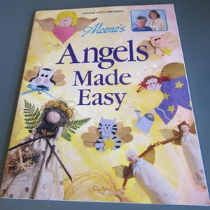 May include: A softcover craft book titled Leisure Arts Presents Aleene's Angels Made Easy. The cover features a yellow background with various handmade angel figures, including a cat angel, a pig angel, and a doll with a floral dress.