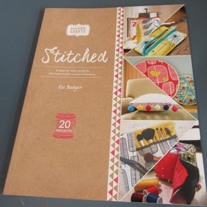 May include: A softcover book titled Stitched: A step-by-step guide to the fashionable world of sewing by Ros Badger. The brown cover features the Maker Crafts logo, a red spool icon with 20 projects, and a collage of various sewn items.
