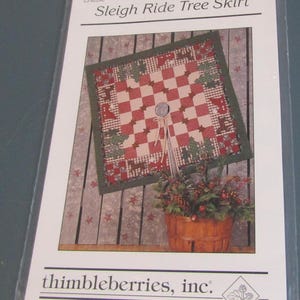 May include: A packaged Christmas tree skirt pattern. The design features a red and white checkered pattern with green trim and Christmas tree accents. The package is labeled "Sleigh Ride Tree Skirt."