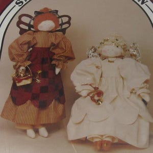 May include: Two handmade angel dolls. One doll wears a brown and red striped dress with a red checkered skirt and carries a basket. The other doll wears a white dress and has a halo and wings.