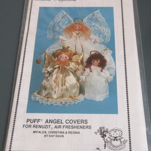 May include: A craft pattern packet titled Atlanta Puffections Puff Angel Covers for Renuzit Air Fresheners by Kay Davis. The cover features three angel dolls with varied hair colors and outfits, including white lace and gold satin fabrics.