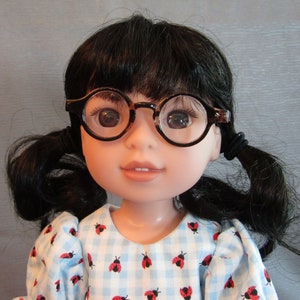 May include: A doll with black hair in pigtails wearing a blue and white gingham dress with red ladybugs. The doll is wearing brown framed glasses.