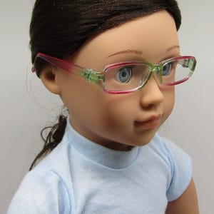 May include: A doll wearing a light blue shirt and pink and green glasses.