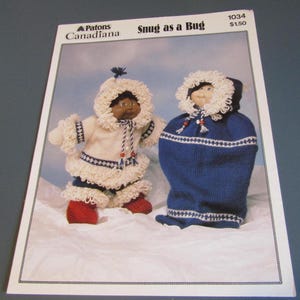 May include: A printed pattern for knitted dolls, featuring two dolls in winter outfits. One doll is standing in a white and blue outfit with red boots. The other doll is in a blue sleeping bag-like garment. The text "Snug as a Bug" is visible.