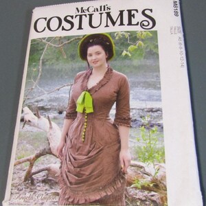 May include: McCall's Costumes sewing pattern featuring a woman in a brown Victorian-era dress with a green bow and hat. The pattern cover includes the text "COSTUMES" and "Angela Clayton". The size is A5 (16-18-10-12-14).