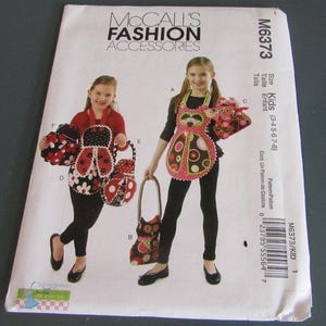 May include: A McCall's Fashion Accessories sewing pattern, M6373, featuring children's aprons and matching bags. The pattern includes sizes for kids aged 3-8. The aprons and bags have ladybug and owl designs. The pattern is printed on white paper.