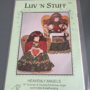 May include: A craft pattern package titled Luv 'N Stuff #HA Heavenly Angels, featuring a 19" Victorian & Country Christmas Angel card holder & wallhanging. The cover shows two fabric angel dolls with dark hair, red and green dresses, and wings.