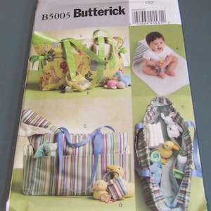 May include: A sewing pattern for baby items, including diaper bags and accessories. The pattern features various bag designs with colorful fabrics, animal prints, and striped patterns. A baby is shown on a changing pad.