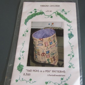 May include: A sewing pattern packet titled THREAD CATCHER A 101 and TWO PEAS IN A POD PATTERNS # A101 C/hartzell/wendel/2001. The cover features a green pea vine illustration and a photograph of a fabric thread catcher with a sewing supply print.