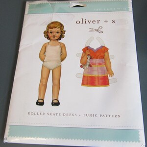 May include: A sewing pattern envelope for a Roller Skate Dress + Tunic by oliver + s. The packaging features an illustration of a paper doll figure and a separate dress graphic with scissors, including sizes 5, 6, 7, 8, 10, and 12 printed at the top.