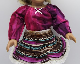 May include: A doll wearing a pink and purple patterned blouse with a white bow, a brown and purple patterned skirt with white lace trim, and brown boots with fringe.