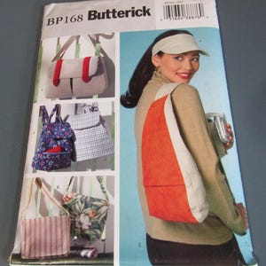May include: A sewing pattern for various bags, including a shoulder bag with an orange front and a beige strap. Other bag designs include a floral print tote, a striped tote, and a backpack. The pattern is labeled "BP168 Butterick".
