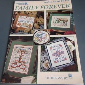 May include: A leaflet titled "Family Forever" featuring cross-stitch designs. The cover displays framed samplers with family-themed quotes and images, including a tree, hearts, and the words "Welcome" and "Family is Love."