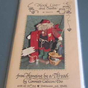 May include: A craft pattern titled "Hook, Line and Santa" featuring a Santa Claus doll dressed in red and black, holding a fishing rod with fish. The pattern is from "Hanging by a Thread" and is 16 inches tall.