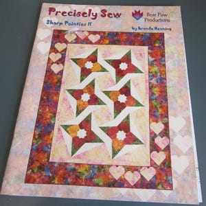 May include: A sewing pattern titled "Precisely Sew Sharp Pointies II" by Brenda Henning. The cover features a colorful quilt design with star-shaped blocks in red, orange, and green, framed by a border with hearts and floral patterns.