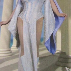 May include: A fantasy-themed costume featuring a white and light blue dress with a textured pattern. The dress has long, flowing sleeves with blue accents and is paired with matching boots. The model has light purple hair.