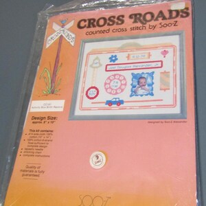 May include: A cross-stitch kit in a plastic package. The kit features a design of a baby's birth record with a photo, a car, and a telephone. The package reads "CROSS ROADS" and "counted cross stitch by Soo-Z". The design size is approximately 8" x 10".