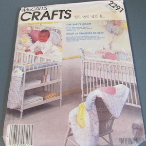 May include: A McCall's Crafts sewing pattern envelope numbered 2291, featuring illustrations of nursery items including a crib, a changing table, a wall hanging, a quilt, a pillow cover, a crib bumper, a diaper stacker, and a crib toy.