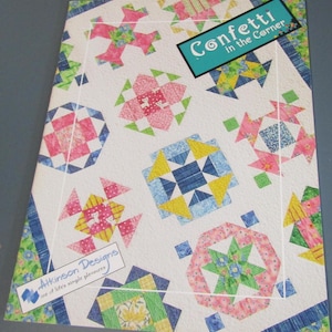 May include: A quilt pattern booklet titled Confetti in the Corner by Atkinson Designs. The cover features a white background with various colorful geometric quilt block designs in shades of pink, blue, yellow, and green, arranged in a scattered layout.