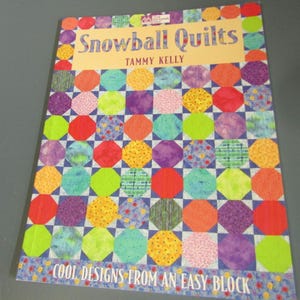 May include: A softcover instructional book titled Snowball Quilts by Tammy Kelly. The cover features a colorful grid of octagonal fabric patches in shades of red, yellow, green, purple, and blue, with the subtitle Cool Designs From An Easy Block.