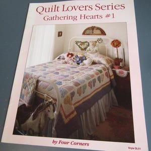 May include: A printed pattern titled "Quilt Lovers Series Gathering Hearts #1" features a bed with a heart-patterned quilt. The bed has a white metal frame, a ruffled bed skirt, and decorative pillows. A rocking horse is at the foot of the bed.