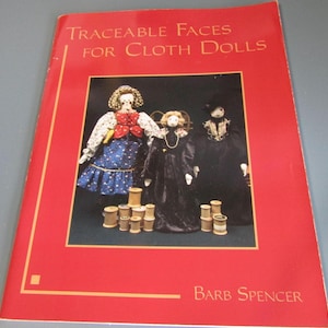 May include: A red book titled "Traceable Faces for Cloth Dolls" by Barb Spencer. The cover features a photo of three cloth dolls with spools of thread. The dolls are dressed in various outfits, including a blue dress with white stars.