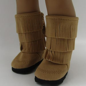 May include: A pair of brown suede boots with fringe detailing. The boots have a zipper on the side and a black sole.
