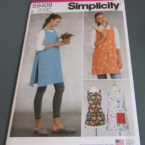 May include: Simplicity sewing pattern S9409 featuring four apron designs. The pattern displays a solid blue side-buttoned apron, an orange floral apron, a dark apron with a colorful butterfly print, and a white apron with a kitchen-themed pattern.
