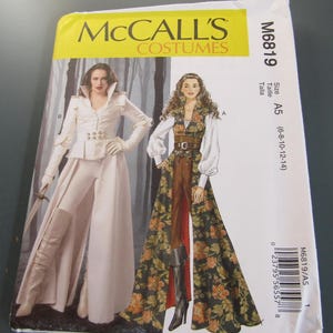 May include: A McCall's Costumes sewing pattern, M6819, featuring two costume designs. One design is a white outfit with a long coat and pants. The other is a floral patterned dress with a brown bodice. The pattern size is A5 (6-8-10-12-14).