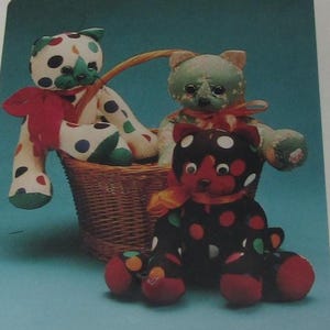 May include: Three handmade teddy bears with polka dots and red accents. One bear is white with colorful polka dots, another is black with red and white polka dots, and the third is green with floral accents. They are in a wicker basket.
