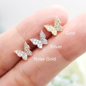 May include: Three butterfly-shaped stud earrings in gold, silver, and rose gold. Each earring is encrusted with small, clear crystals. The colors are labeled: Gold, Silver, and Rose Gold.