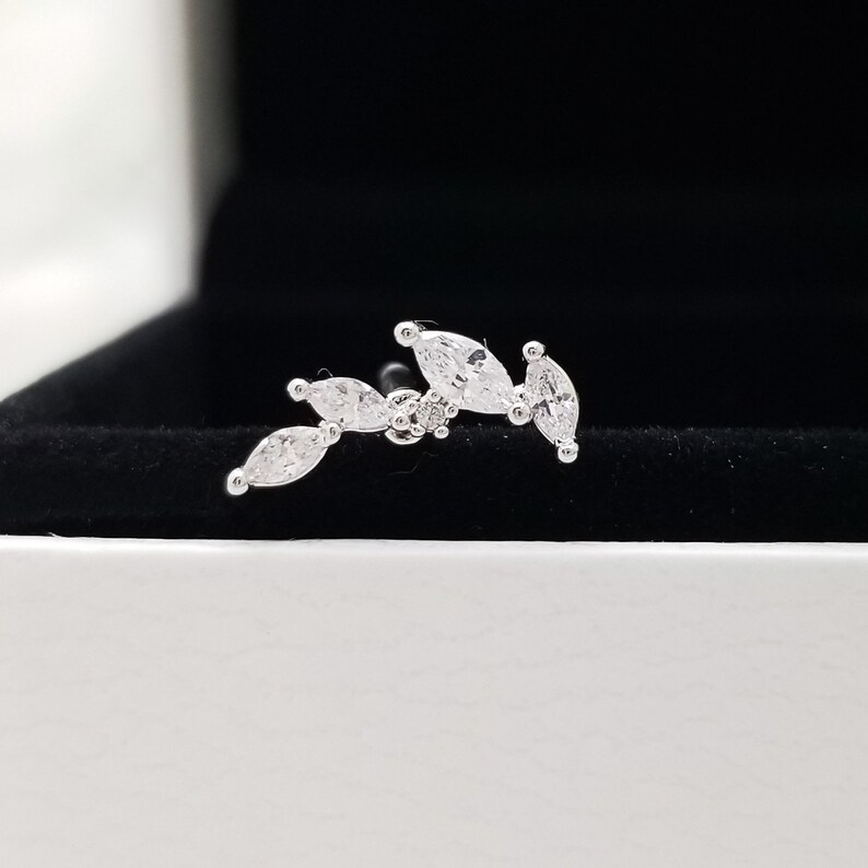 May include: A silver ear cuff with a row of marquise-shaped clear cubic zirconia stones.