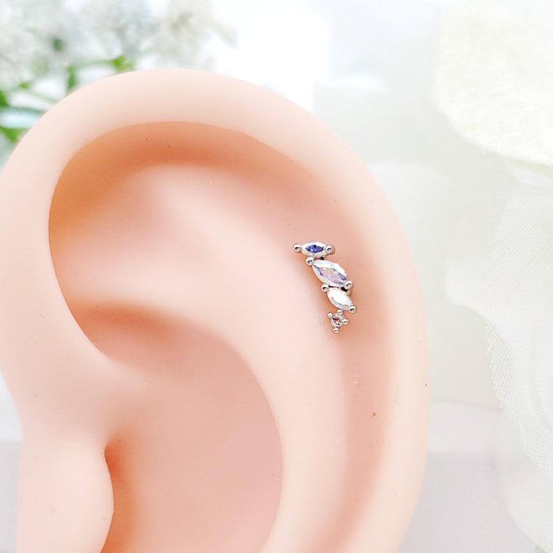 May include: A silver ear piercing with a row of four clear marquise-shaped gemstones.