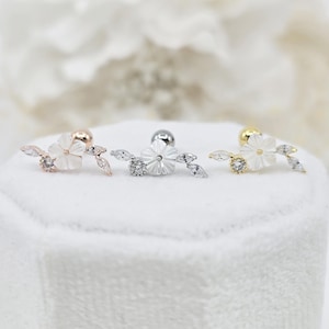 Peut inclure: Trois boucles d'oreilles en forme de fleur en or rose, argent et or. Chaque boucle d'oreille présente une fleur centrale avec un centre de pierres précieuses et des accents en forme de feuille. Les boucles d'oreilles sont exposées sur une surface blanche.