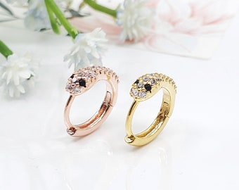 May include: Two snake-shaped hoop earrings with black and white cubic zirconia stones. The earrings are available in gold and rose gold.