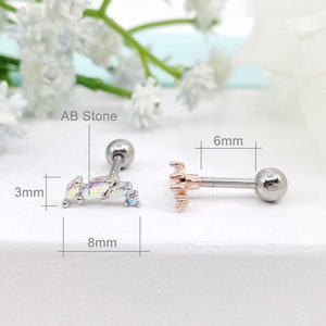 May include: Two silver barbell earrings with clear AB stones. The earring on the left has a row of five stones, and the earring on the right has a cluster of stones. The earrings are 6 mm in diameter and 8 mm in length.