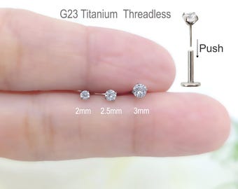 May include: Three sizes of clear gem titanium threadless push-in stud earrings. The earrings are 2mm, 2.5mm, and 3mm in diameter. The earrings are shown on a person's finger.