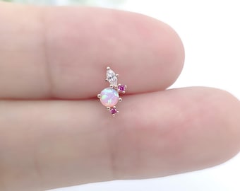 May include: A small, rose gold-toned earring featuring a cluster of gemstones. The design includes a central, round, opalescent stone, a marquise-cut clear stone, and several small, round, pink gemstones. The earring is designed for a single piercing.
