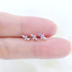 May include: Three silver-toned earrings, each with a floral design. The earrings feature iridescent, petal-shaped stones and small, clear accent stones. The earrings are displayed on a light background.