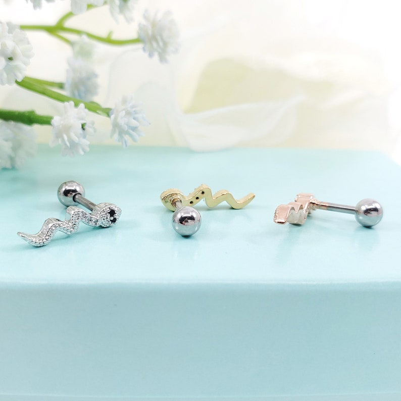 May include: Three silver, gold, and rose gold snake cartilage earrings with a ball end. The snake designs are different on each earring.