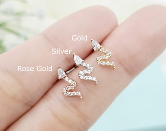 May include: Three snake-shaped stud earrings in rose gold, silver, and gold tones. Each earring features a pear-cut clear stone for the head and a winding body encrusted with small clear stones. The text labels Rose Gold, Silver, and Gold are visible.