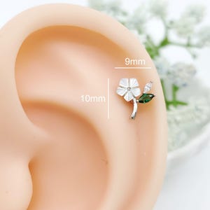 May include: A silver-toned flower earring stud featuring a white petal design, a clear marquise-cut stone, and a green marquise-cut stone. The earring measures 9mm in width and 10mm in height, as indicated by the text labels on the image.